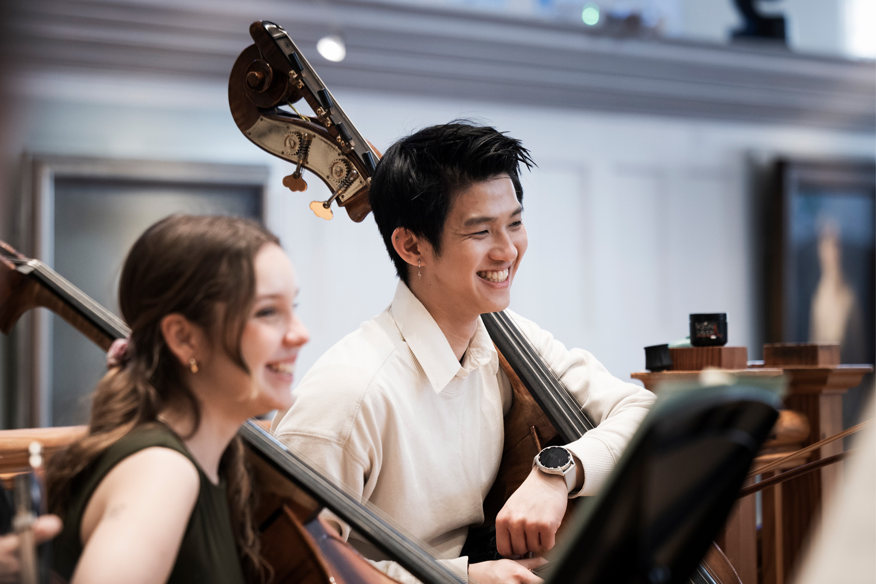 Double bassists smiling while holding their double basses, in an orchestra rehearsal. Double bassists smiling while holding their double basses, in an orchestra rehearsal.